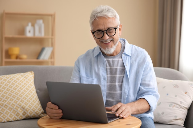 Hombre mayor usando una computadora portátil en una mesa de madera en el interior