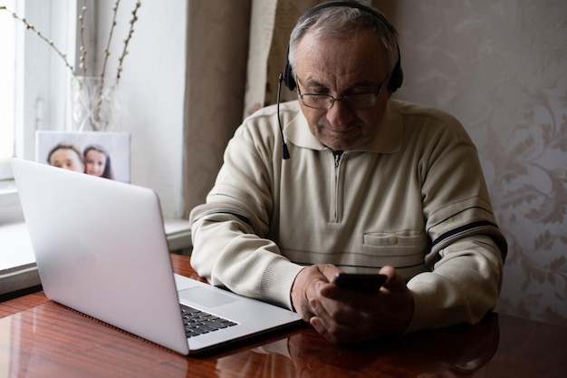 Hombre mayor usando laptop y auriculares en línea.