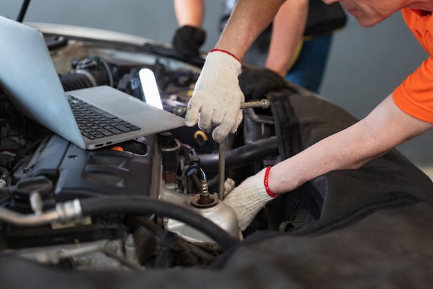 Hombre mecánico con herramienta de llave inglesa con portátil, control y mantenimiento de reparación del motor en el garaje de servicio automático