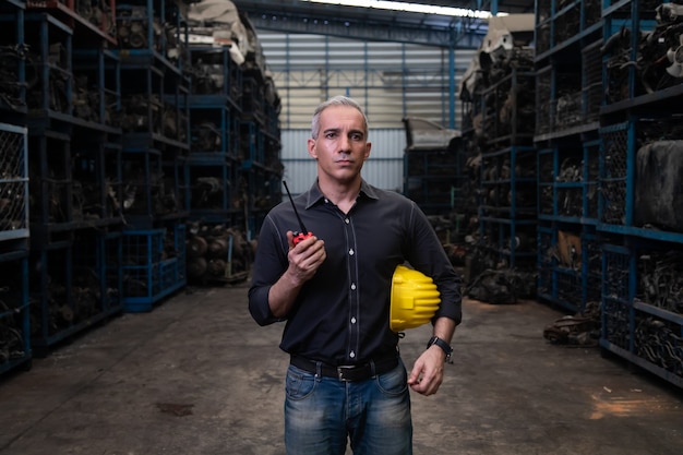 Hombre mecánico propietario de una pequeña empresa que inspecciona el stock de piezas de automóviles viejos en una computadora portátil mientras trabaja en un gran almacén de piezas de automóviles viejos