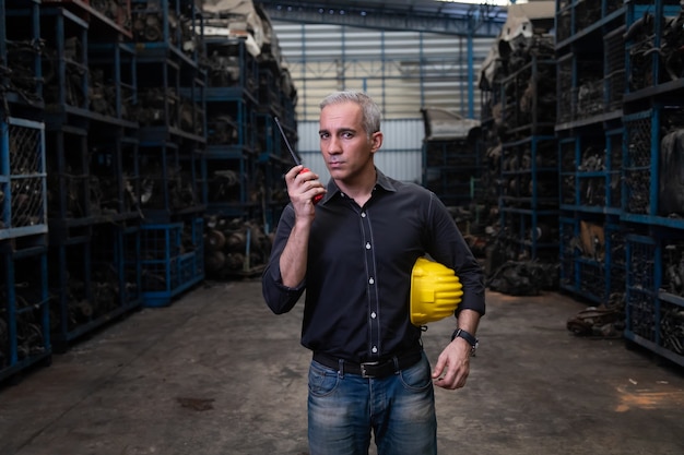 Hombre mecánico propietario de una pequeña empresa que inspecciona el stock de piezas de automóviles viejos en una computadora portátil mientras trabaja en un gran almacén de piezas de automóviles viejos