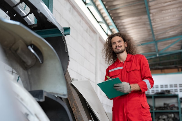 Foto hombre mecánico sonriente sosteniendo un clipboard comprobando parte del coche para repararlo en el servicio de garaje