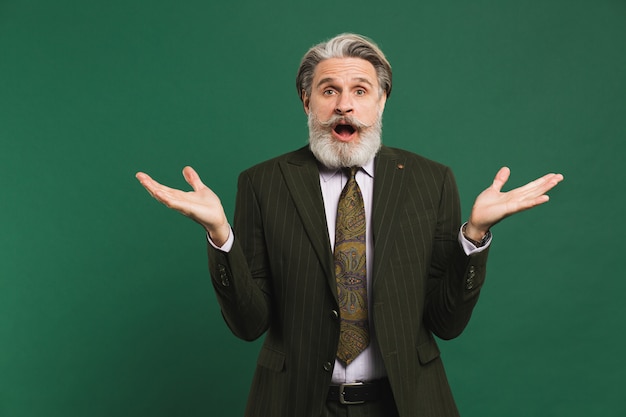 Hombre de mediana edad con barba en traje agitando sus manos a un lado en una pared verde con espacio de copia.