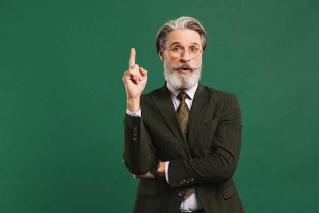 Hombre de mediana edad con barba en traje levanta el dedo índice y muestra la idea en la pared verde con espacio de copia