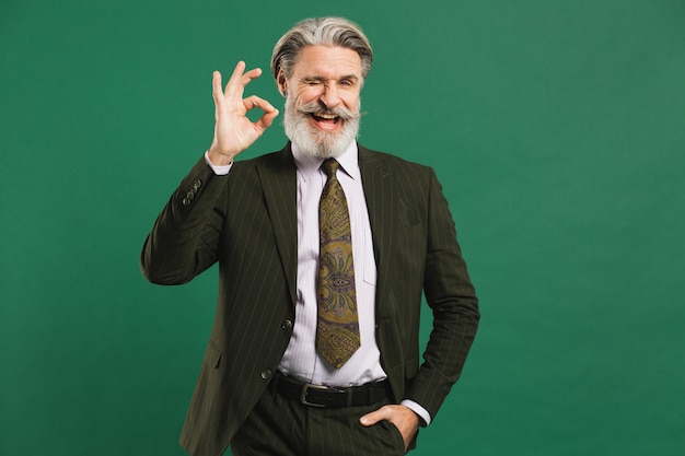 Hombre de mediana edad con barba en traje muestra bien en la pared verde con espacio de copia.