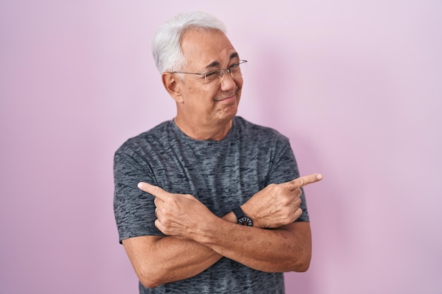 Hombre de mediana edad con cabello gris parado sobre fondo rosa apuntando a ambos lados con los dedos en diferentes direcciones en desacuerdo