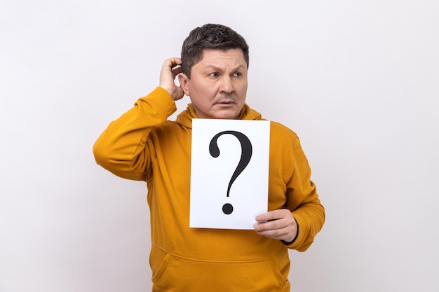 Hombre de mediana edad con cabello oscuro mirando hacia otro lado sosteniendo papel con signo de interrogación piensa en tareas