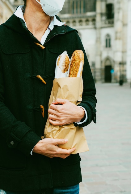 Foto hombre de mediana edad en la calle con pan, baguette, compras de pan durante la pandemia mundial, con máscara, obteniendo pan de la panadería. comida para llevar, compras de panadería durante el covid 19.