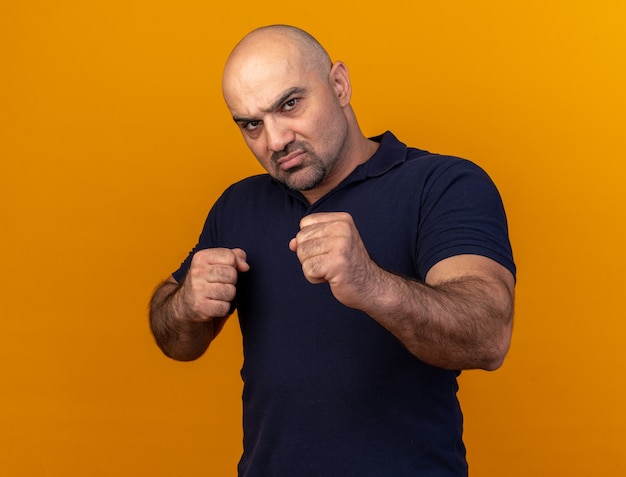 Hombre de mediana edad casual confiado haciendo gesto de boxeo aislado en la pared naranja