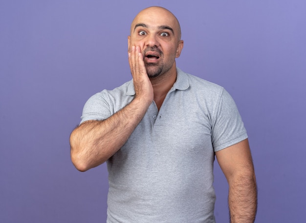 Hombre de mediana edad casual preocupado manteniendo la mano en la cara aislada en la pared púrpura