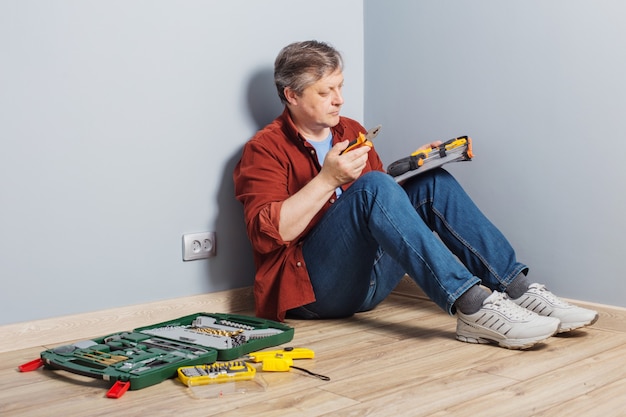 Hombre de mediana edad con un conjunto de herramientas de reparación sobre un piso de madera