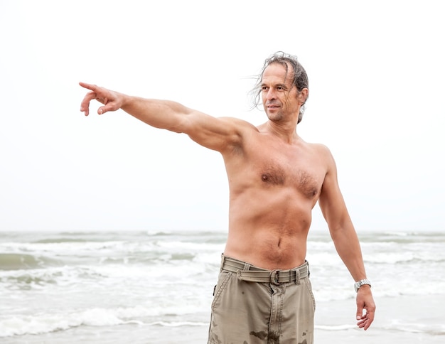 Hombre de mediana edad disfruta de la naturaleza junto al mar y señala algo en la distancia