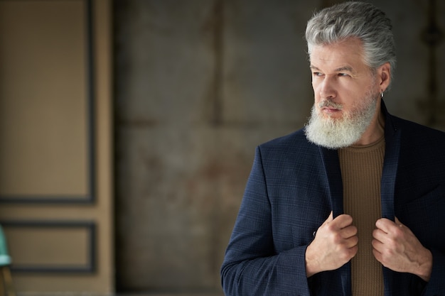 Hombre de mediana edad guapo serio elegante mirando a otro lado ajustando su traje mientras posa en interiores