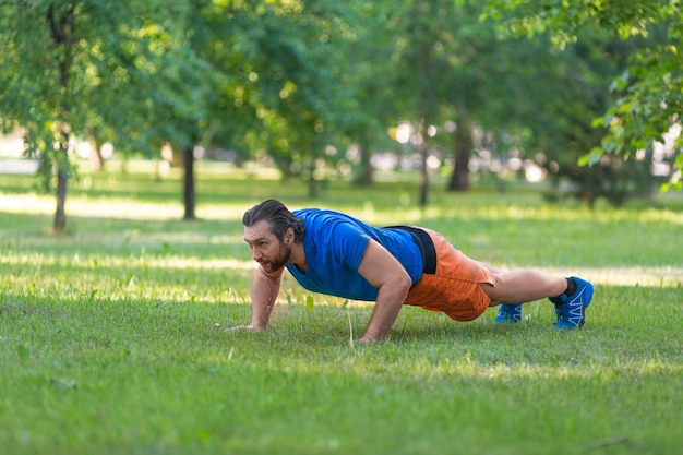 Hombre de mediana edad haciendo flexiones en el césped en el parque