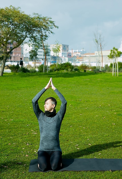 Hombre de mediana edad haciendo respiración, relajación, yoga, estiramiento, ejercicio, entrenamiento en el parque con estera de yoga. Presentación de yoga natural para principiantes. Concepto de salud.