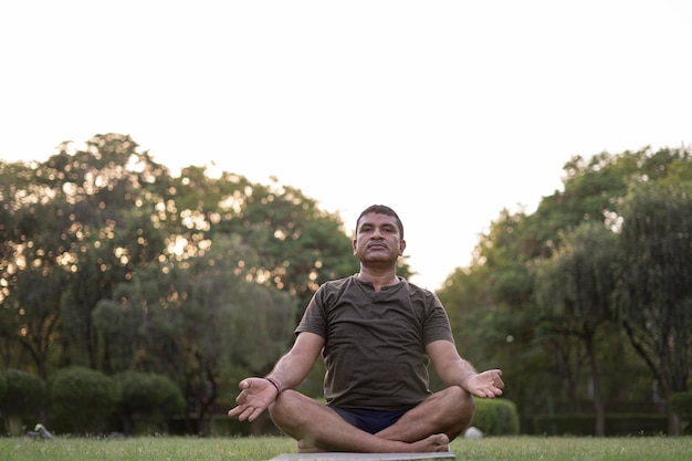 Hombre de mediana edad haciendo yoga en un parque cubierto de árboles en el día internacional del yoga