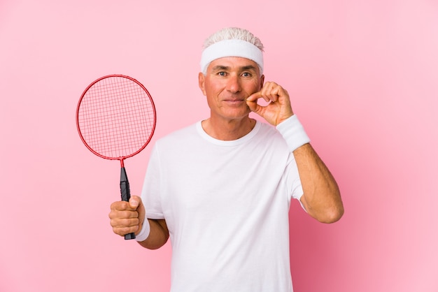 Hombre de mediana edad jugando bádminton aislado con los dedos en los labios manteniendo un secreto.