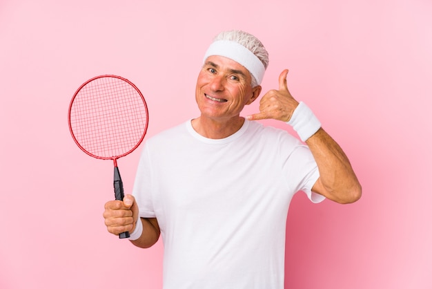 Hombre de mediana edad jugando bádminton aislado mostrando un gesto de llamada de teléfono móvil con los dedos.