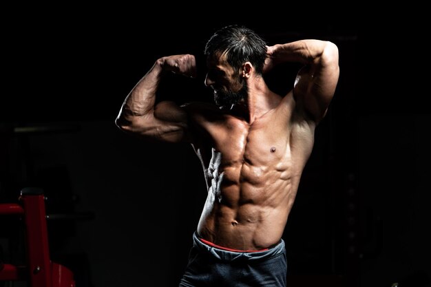Hombre de mediana edad de pie fuerte en el gimnasio y flexionando los músculos - Modelo de fitness culturista atlético muscular posando después de los ejercicios
