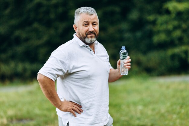 Hombre de mediana edad de pie sosteniendo una botella con agua y mirando.