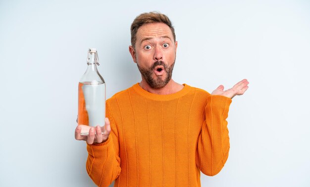 Hombre de mediana edad que parece sorprendido y conmocionado, con la mandíbula caída sosteniendo un objeto. concepto de botella de agua