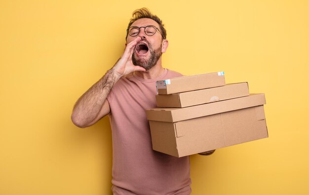 Hombre de mediana edad que se siente feliz, dando un gran grito con las manos al lado de la boca. concepto de cajas de paquetes