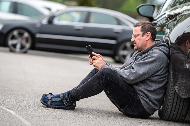 Foto hombre de mediana edad sentado en el asfalto junto al coche y trabajando en una computadora portátil trabajando remotamente persona de viaje