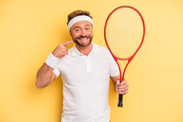 Hombre de mediana edad sonriendo con confianza apuntando a su propia sonrisa amplia. concepto de tenis