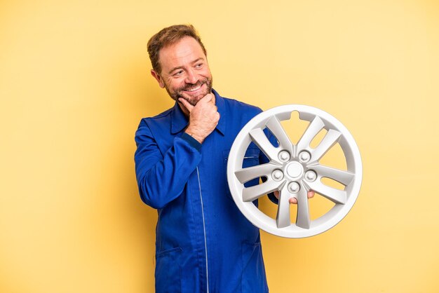 Hombre de mediana edad sonriendo con una feliz expresión de confianza con la mano en el concepto de mecánico de automóviles de barbilla