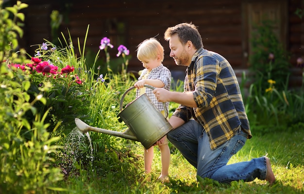 Hombre de mediana edad y su pequeño hijo regando flores en el jardín en un día soleado de verano