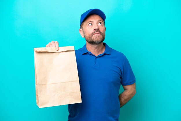 Hombre de mediana edad tomando una bolsa de comida para llevar aislada de fondo azul y mirando hacia arriba