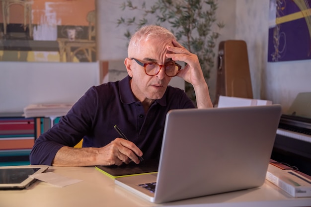 Hombre de mediana edad usando la computadora en su estudio de arte y dibujando en su tableta