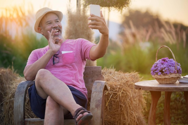 Hombre de mediana edad visita un sitio de citas en línea a través de un teléfono sentado en un jardín de flores, se centra en la mano