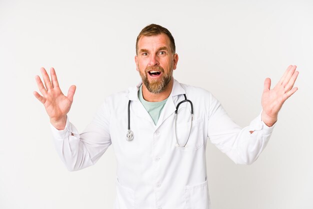 Hombre médico senior aislado en la pared blanca recibiendo una agradable sorpresa, emocionado y levantando las manos.