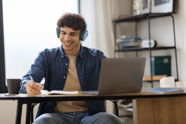 Hombre del medio oriente en la computadora portátil tomando notas con auriculares en el interior