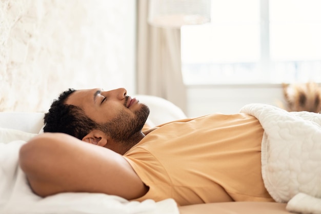 Hombre del Medio Oriente durmiendo acostado en una cama acogedora en el dormitorio