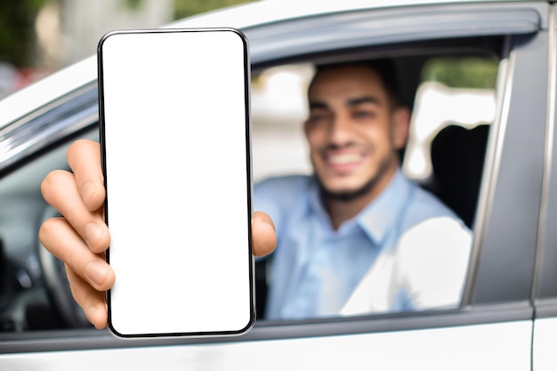 Hombre del medio oriente mostrando teléfono celular con pantalla en blanco mientras está sentado en el auto