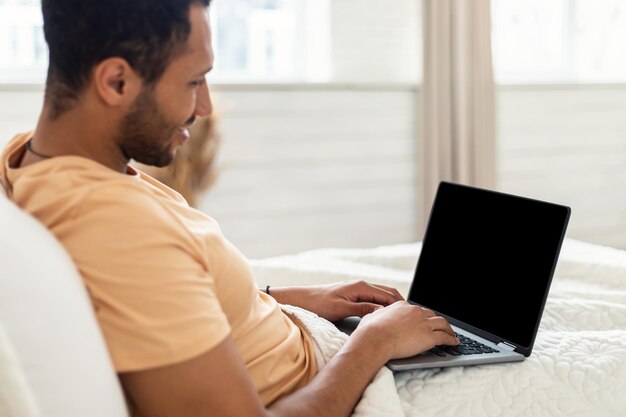 Hombre del medio oriente usando laptop con pantalla vacía en el dormitorio