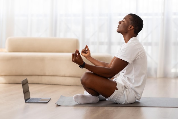 Hombre meditando en casa en una alfombra de yoga