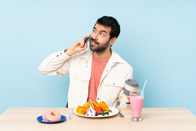 Hombre en una mesa desayunando gofres y un batido con café para llevar y un móvil