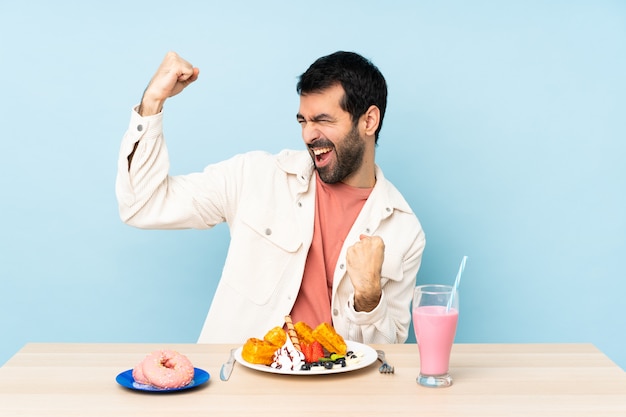 Hombre en una mesa desayunando gofres y un batido celebrando una victoria