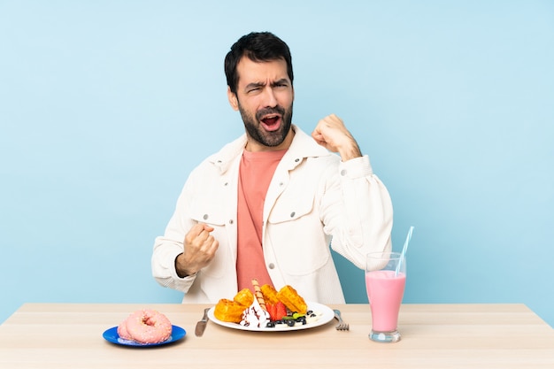 Hombre en una mesa desayunando gofres y un batido celebrando una victoria