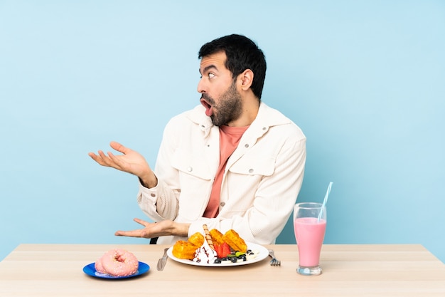 Hombre en una mesa desayunando gofres y un batido con expresión facial sorpresa