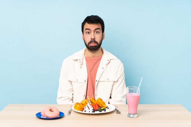 Hombre en una mesa desayunando gofres y un batido con expresión triste y deprimida