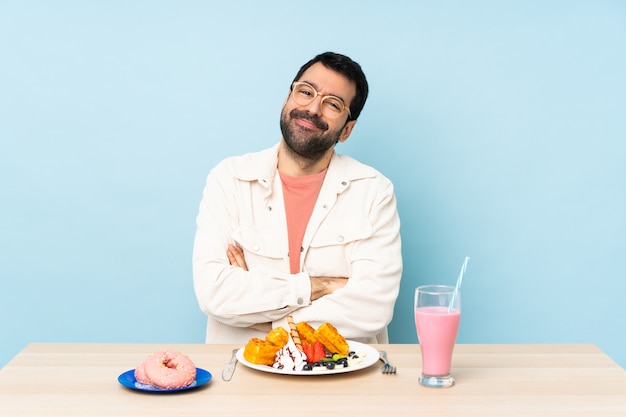 Hombre en una mesa desayunando gofres y un batido con gafas y sonriendo