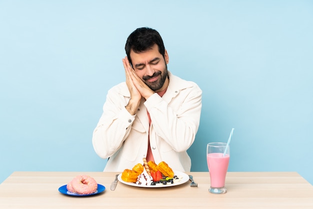 Hombre en una mesa desayunando gofres y un batido haciendo gesto de sueño en expresión dorable