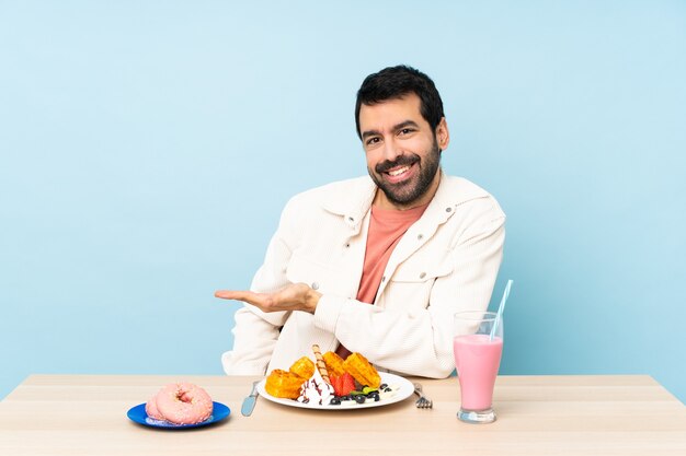 Hombre en una mesa desayunando gofres y un batido presentando una idea mientras mira sonriendo hacia