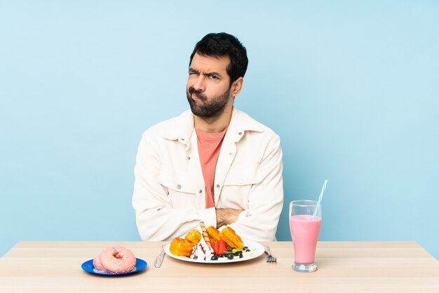 Hombre en una mesa desayunando gofres y un batido sintiéndose molesto