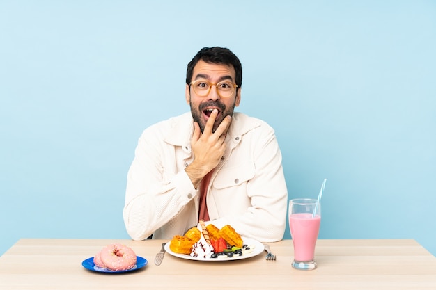 Hombre en una mesa desayunando gofres y un batido con vasos y sorprendido