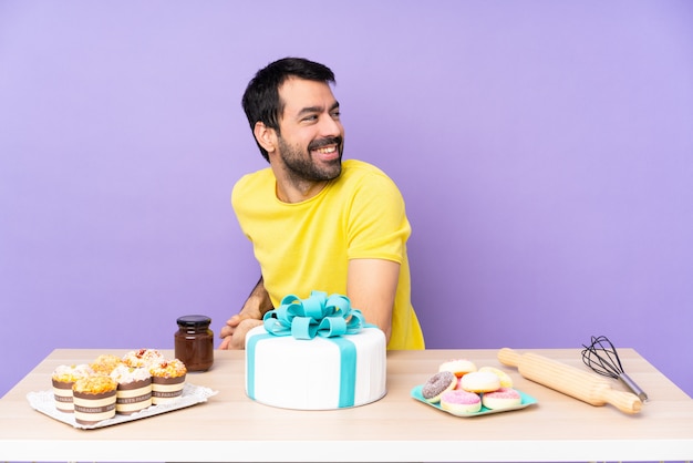 Hombre en una mesa con un gran pastel con los brazos cruzados y feliz